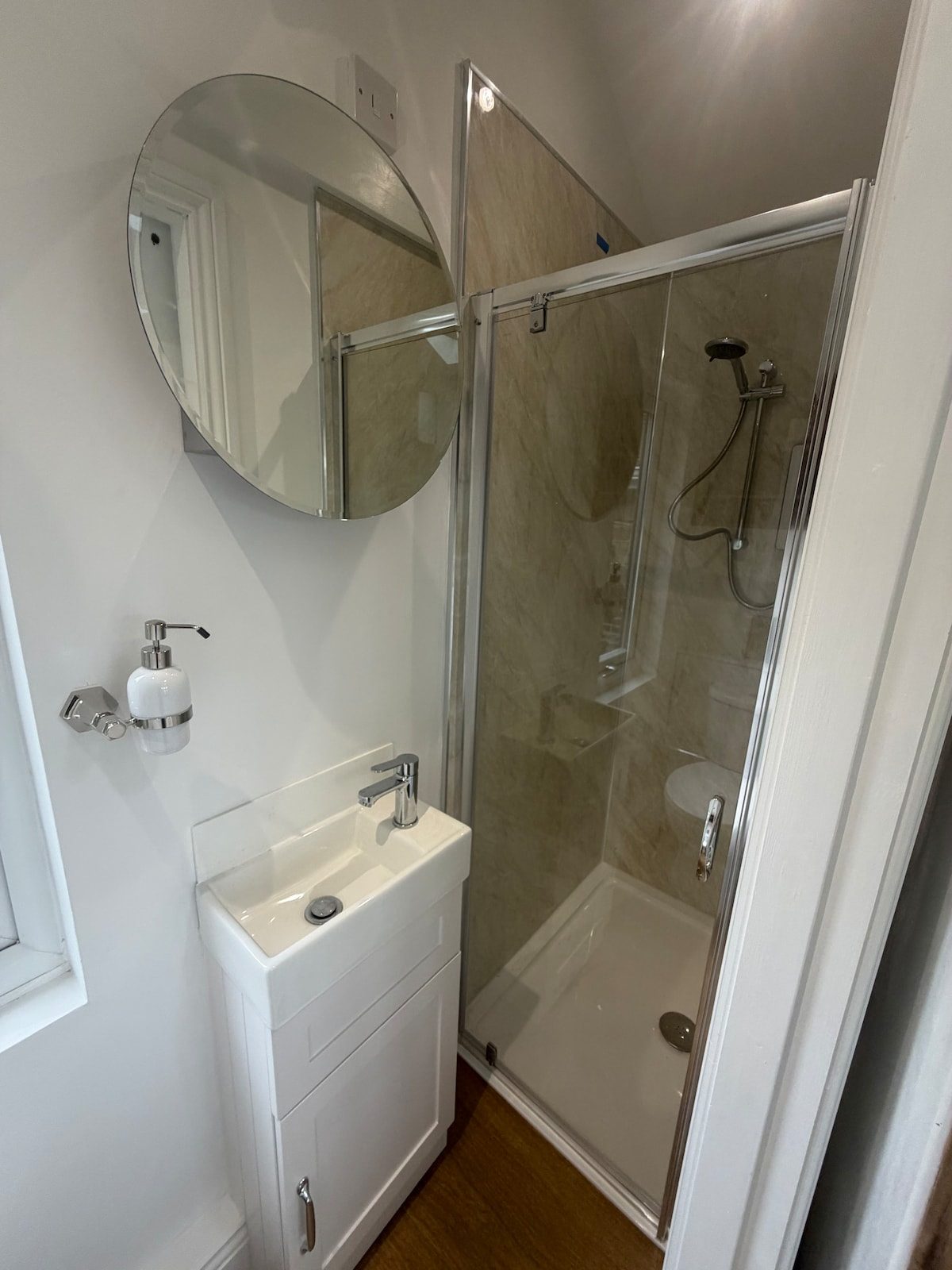 Bathroom with round mirror, basin unit and glass shower enclosure